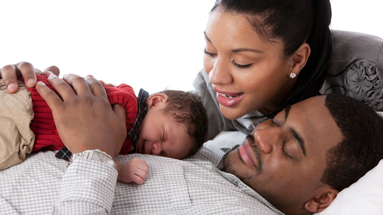 A man and woman are laying on a bed with a baby.