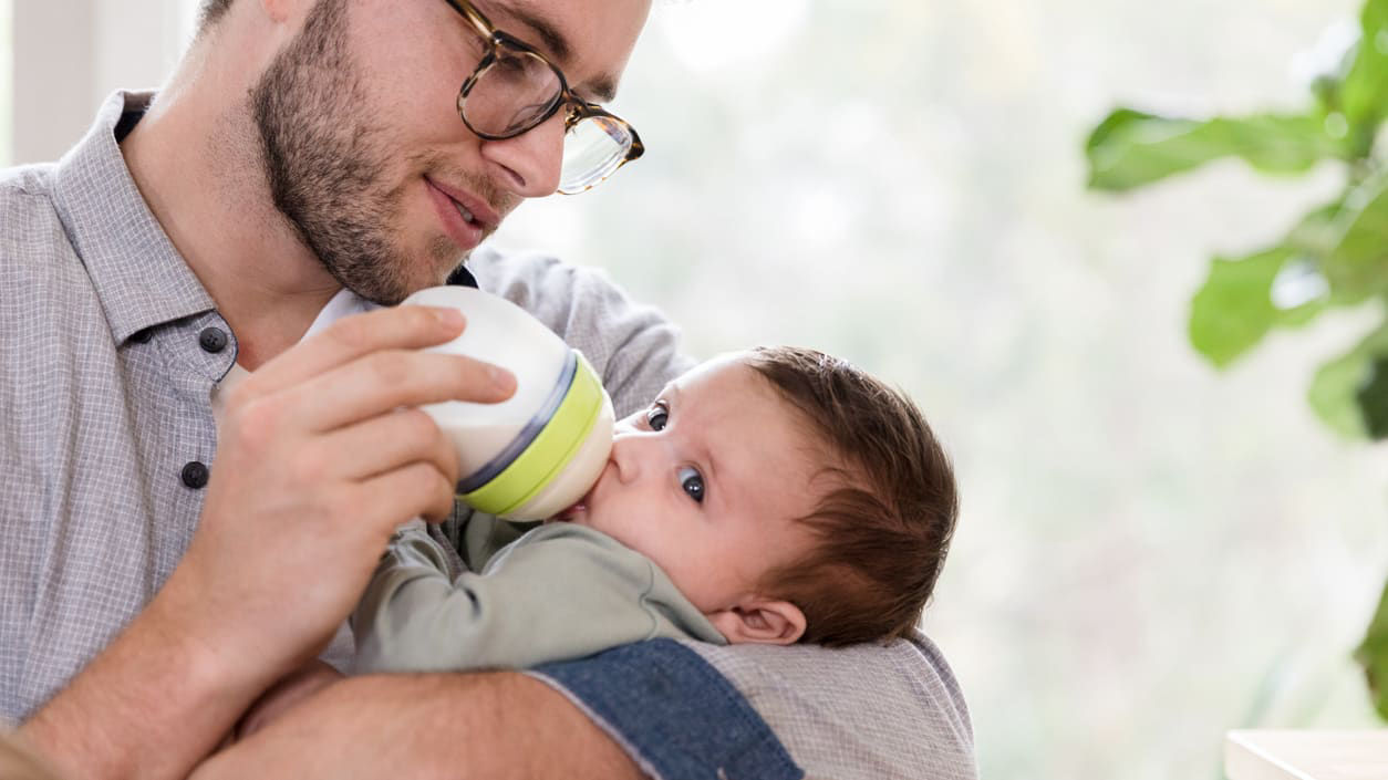 A man is holding a baby while drinking from a bottle.