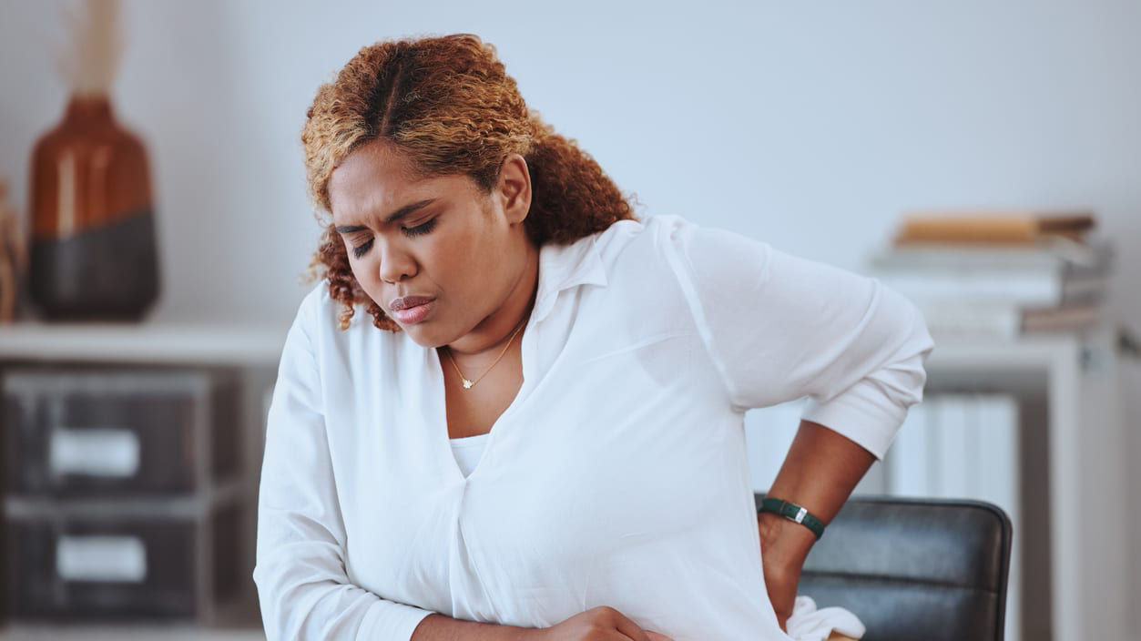 A woman sitting at a desk with her back pain.