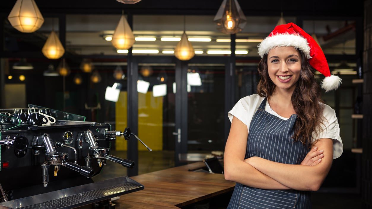 A woman in a santa hat standing in front of a coffee machine.