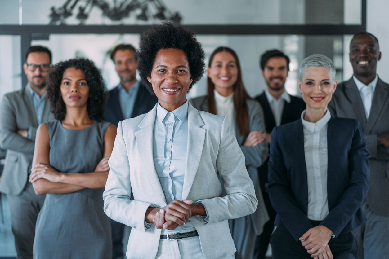 Portrait of beautiful smiling businesswoman with her colleagues. Multi-ethnic group of business persons standing in modern office. Successful team leader and her team in background.