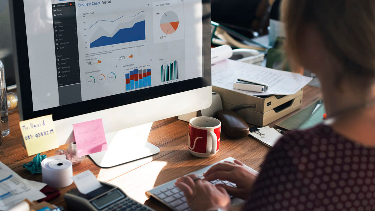 A woman is working on a computer with a graph on the screen.