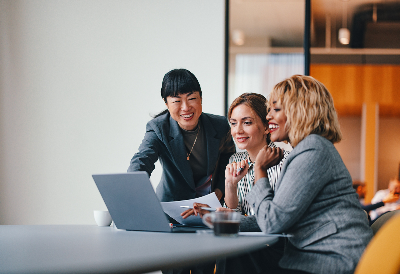 Three smiling multiethnic entrepreneurs using a laptop while making some business analysis.