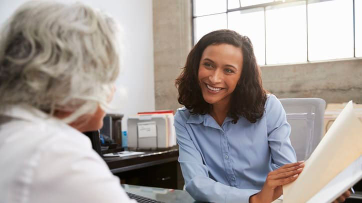 A woman sitting at a desk and talking to a woman.