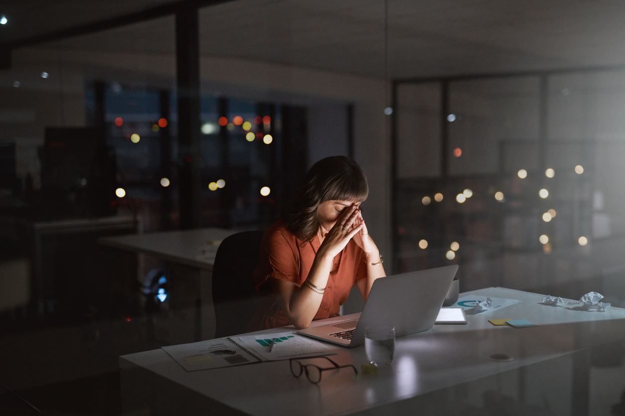 businesswoman looking stressed out while working on a laptop in an office at night