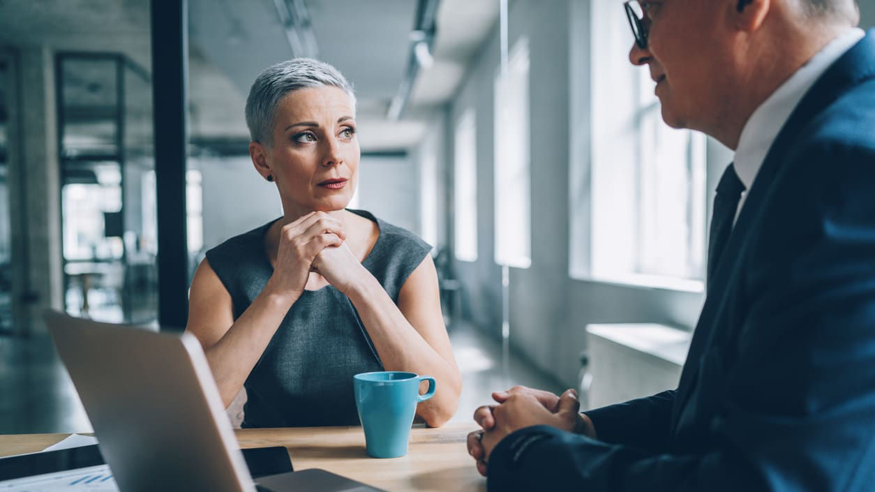 A woman and a man talking at a table in an office.