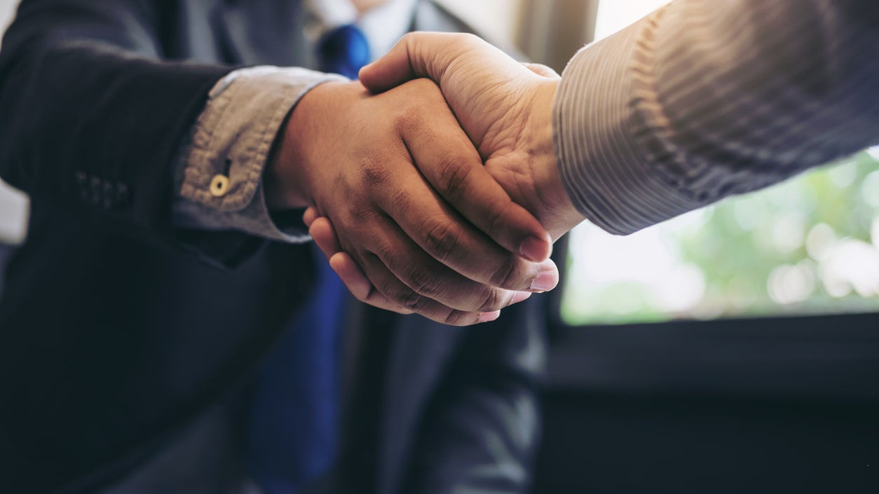 Two businessmen shaking hands in front of a window.