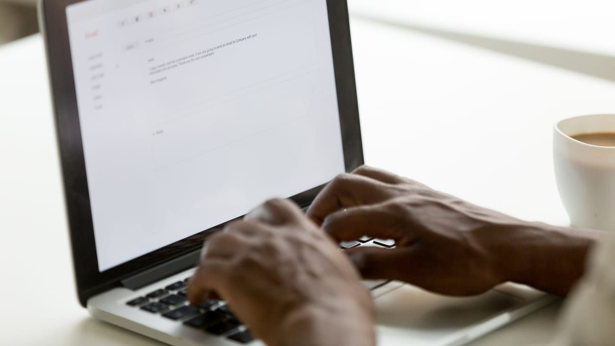 A person typing on a laptop with a cup of coffee.