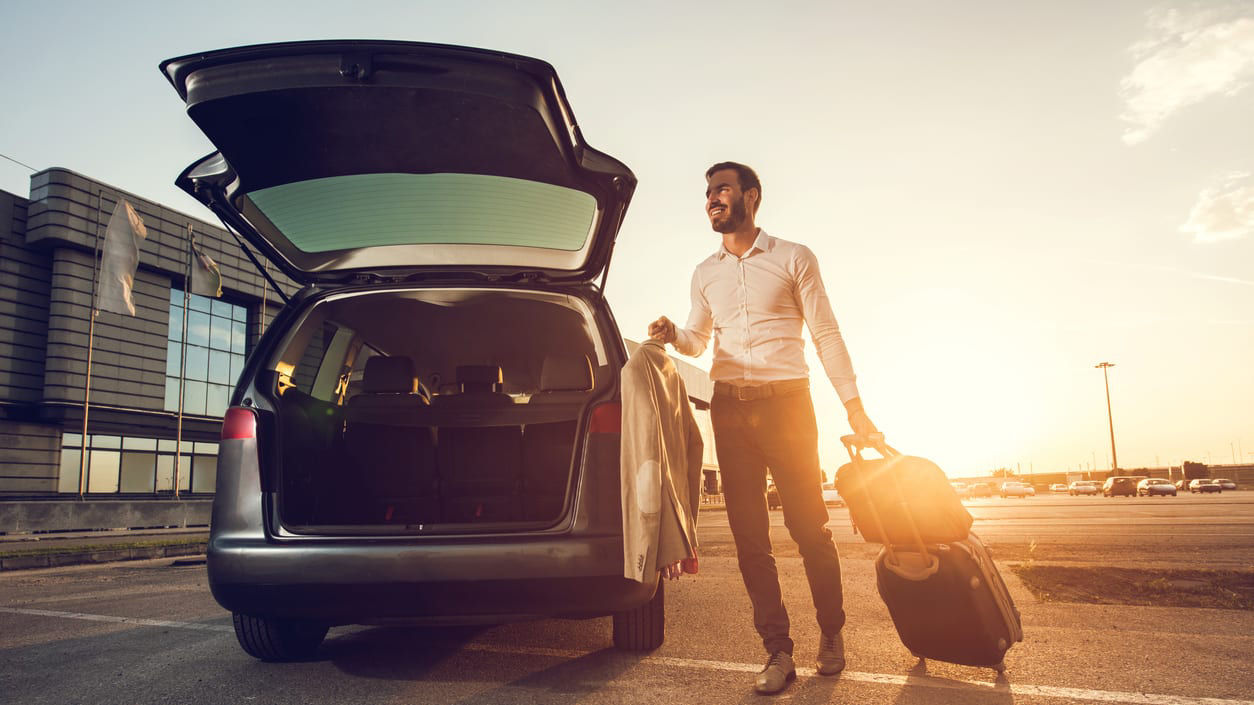 A man is standing next to a car with his luggage.