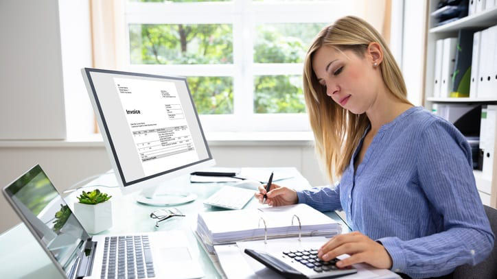 A woman working at her desk with a calculator and laptop.