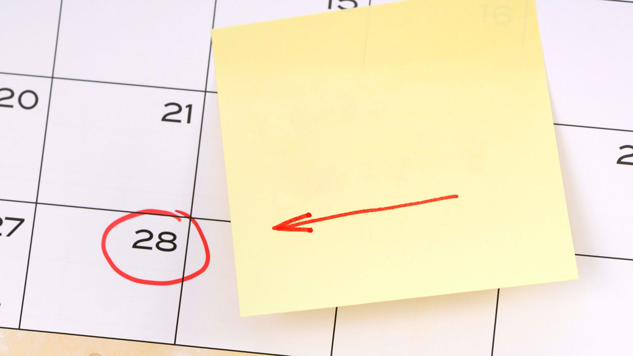 A sticky note with a red arrow on it is on a calendar.