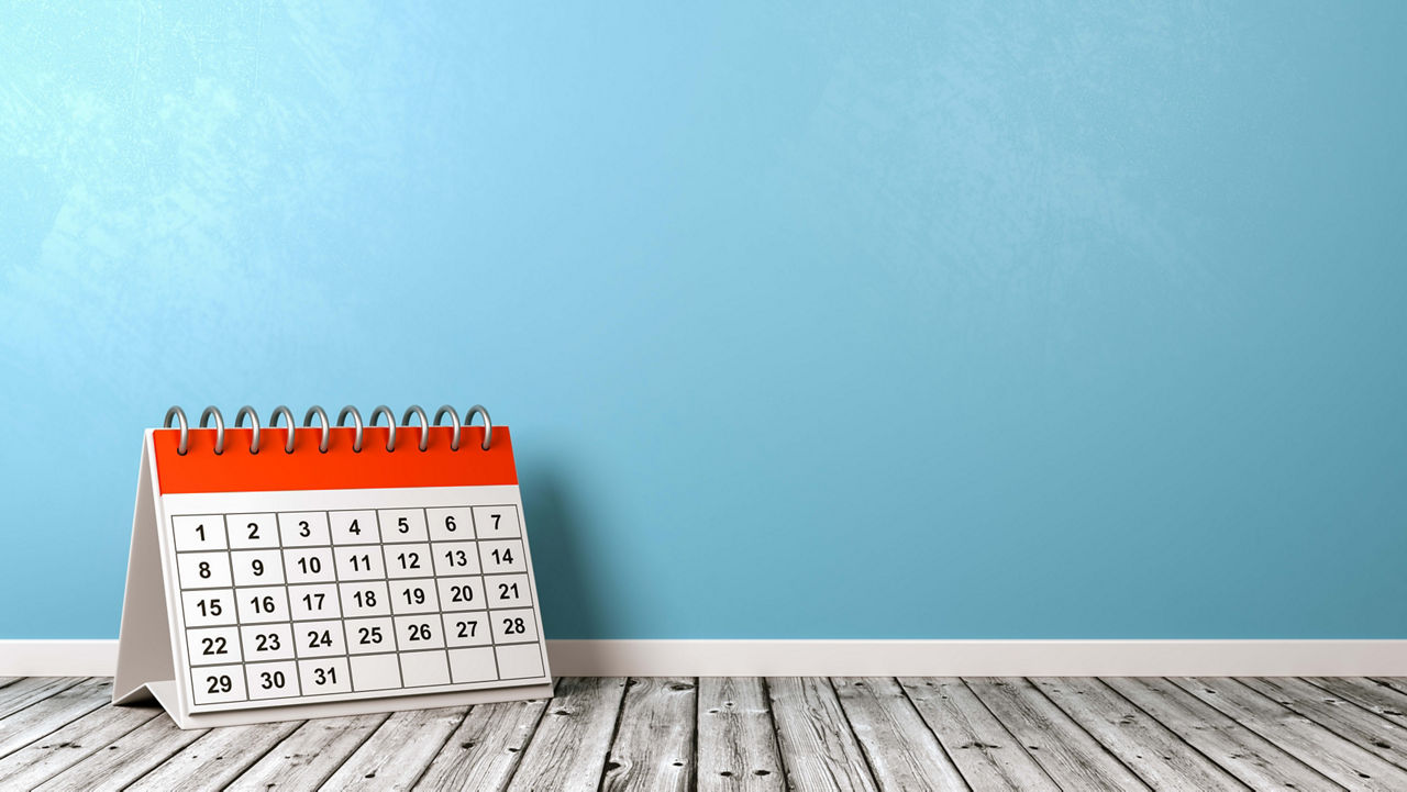 A calendar on a wooden floor in front of a blue wall.