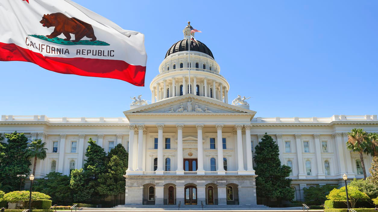 A california flag is flying in front of the california capitol building.