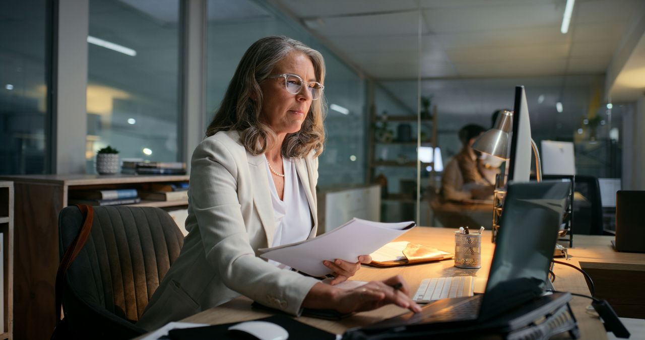 A woman works at night on her laptop to send a financial email to a client.