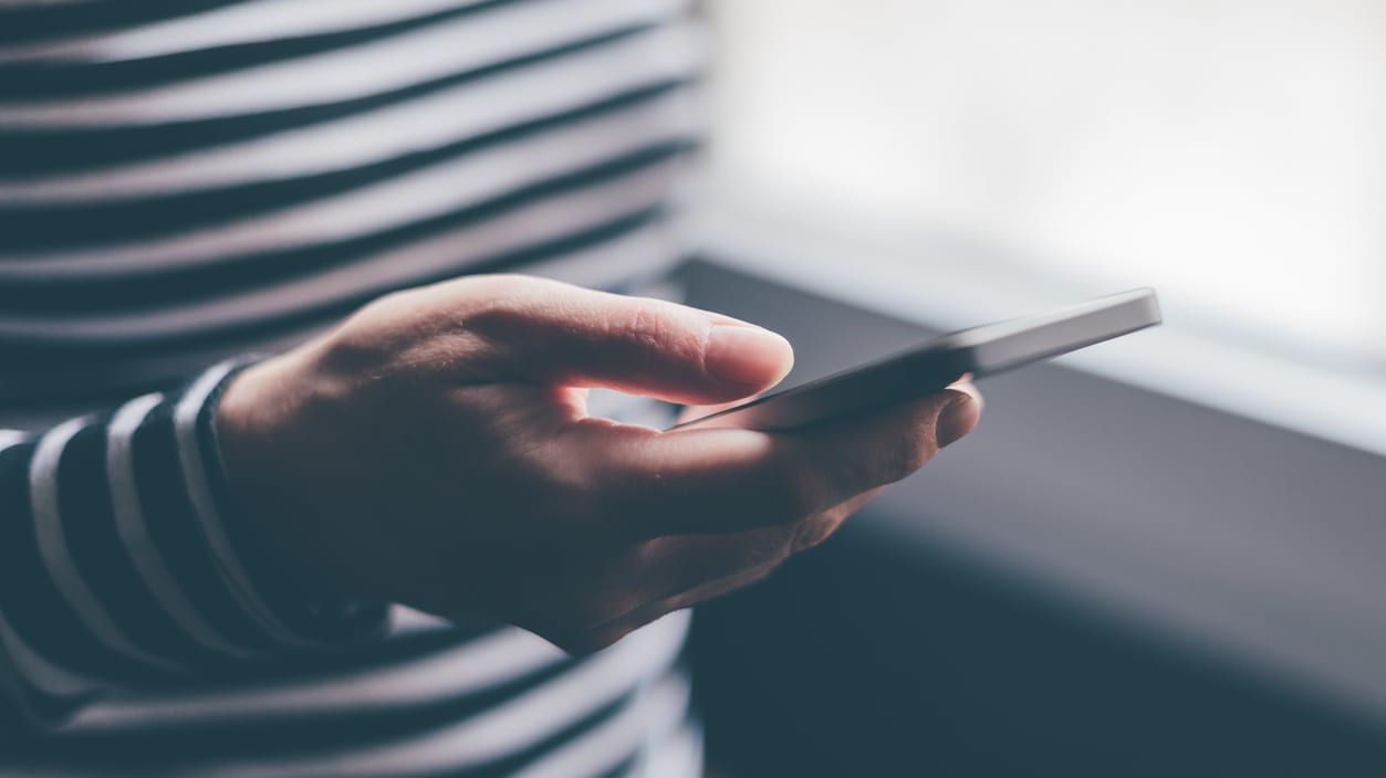A person holding a cell phone in front of a window.