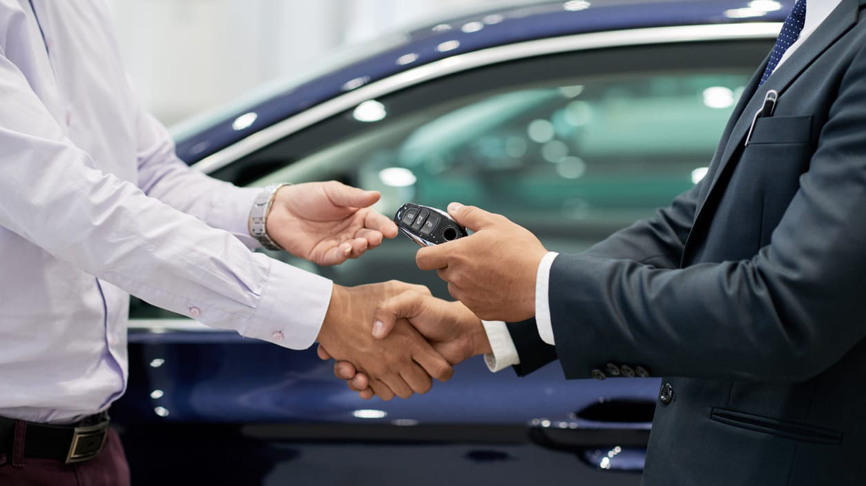 Two men shaking hands in front of a car dealership.