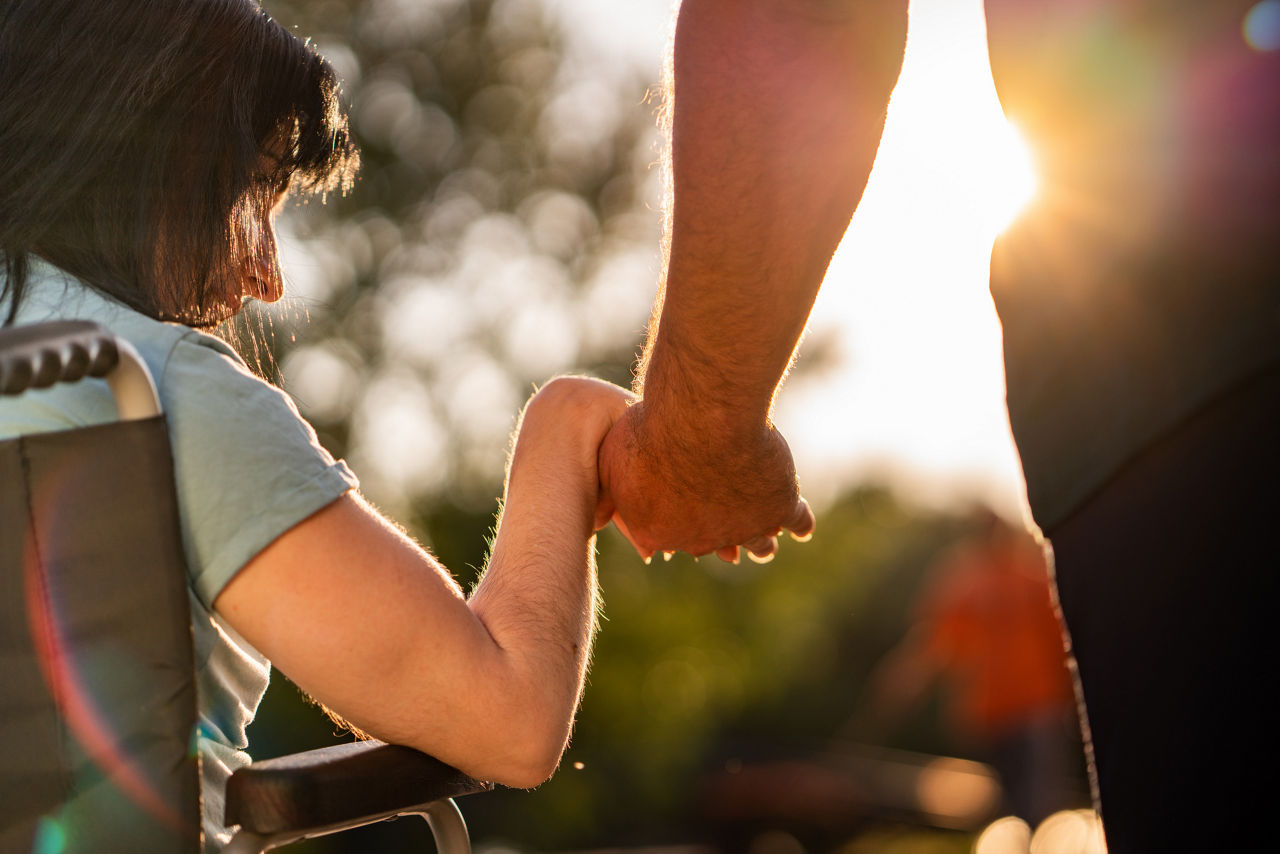 A woman in a wheelchair holds hands with a man, symbolizing support and connection between them.