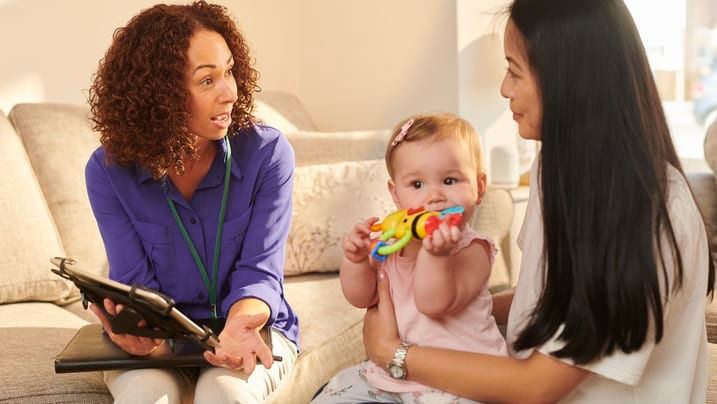 A woman is talking to a baby on a couch.