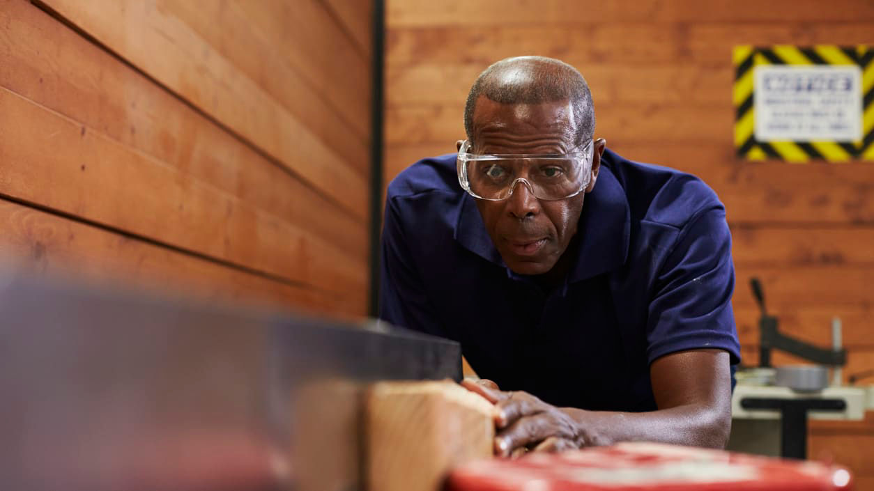 A man in glasses is working on a piece of wood.
