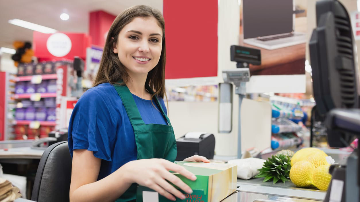 A woman is standing at the register in a grocery store.