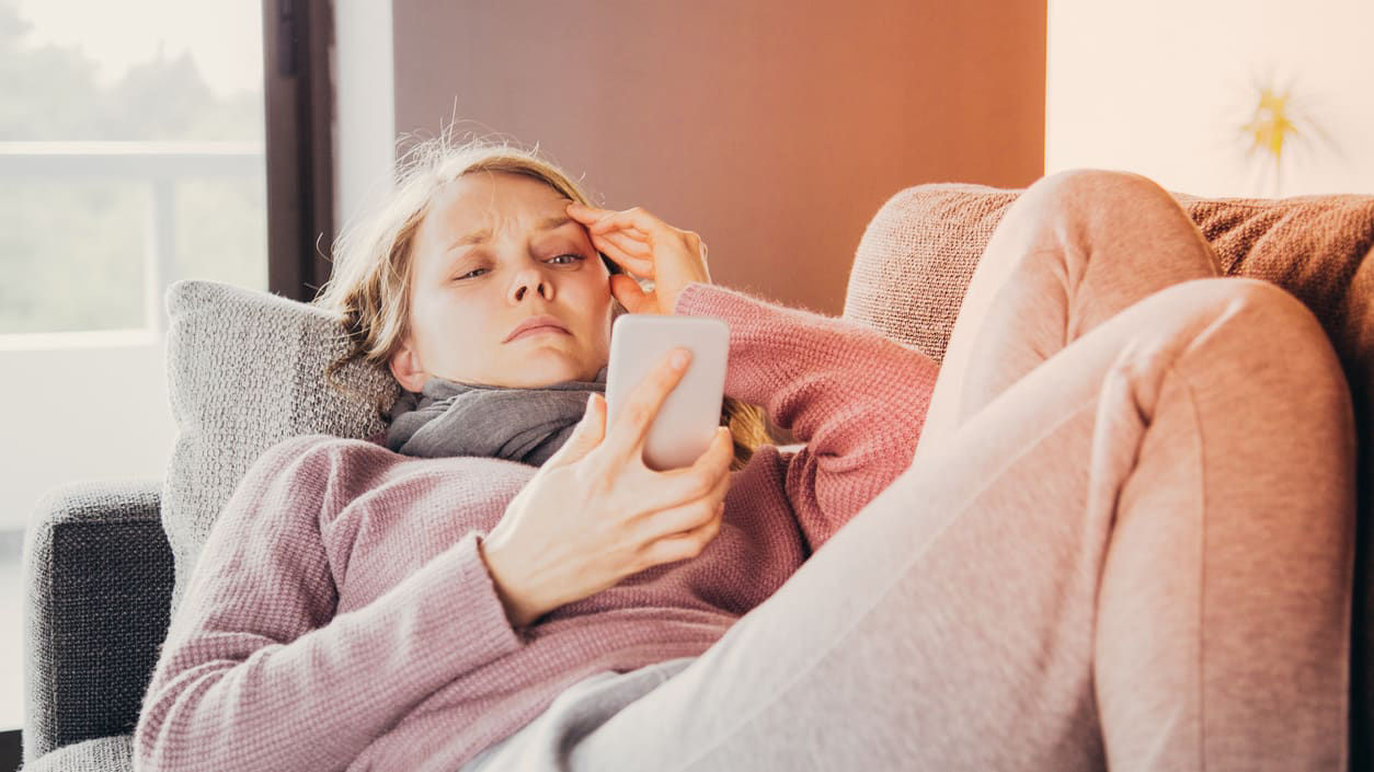 A woman is sitting on a couch looking at her phone.