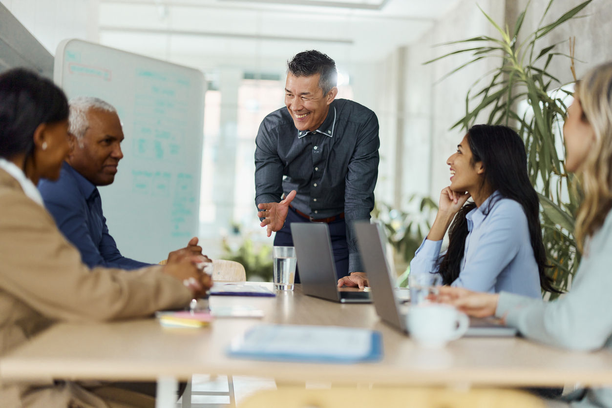 Business leader speaking to a group of four other professionals around a table.