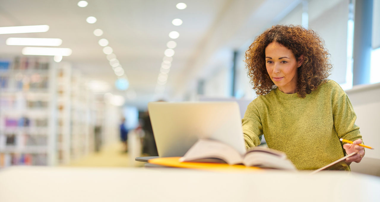 Woman studies in library with laptop and books