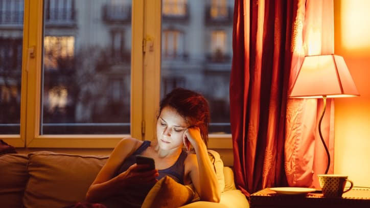 A woman sitting on a couch looking at her phone at night.