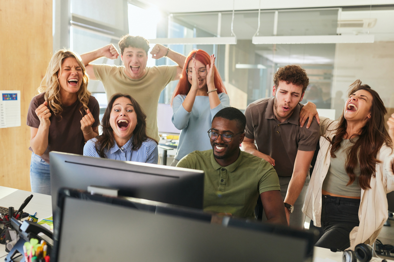 Group of cheerful computer programmers celebrating their achievement while working on PC in the office.