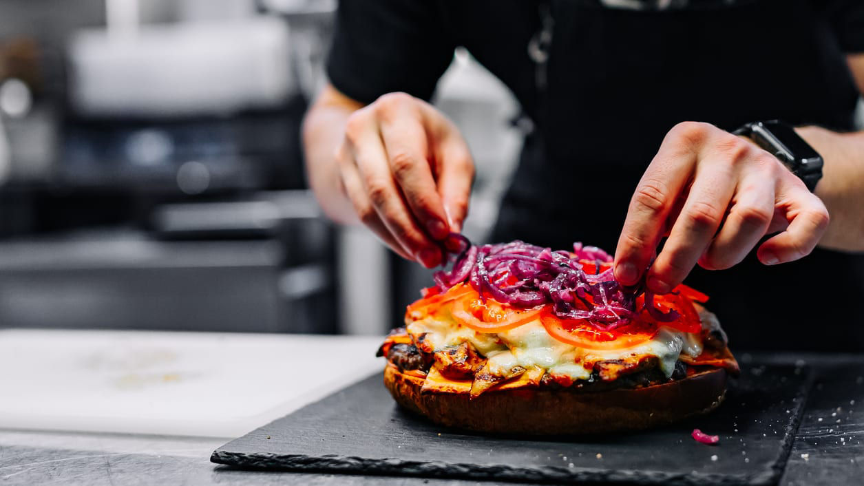 A man is putting toppings on a pizza.
