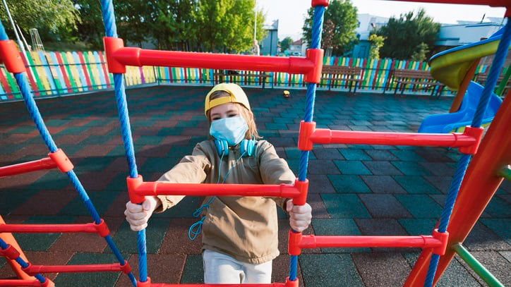 A boy wearing a face mask in a playground.