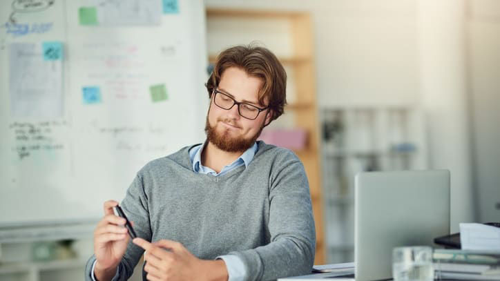 A bearded man sitting at a desk in an office.