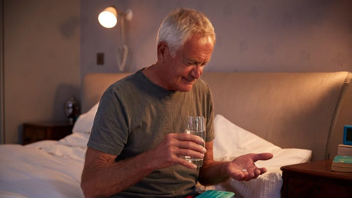 A man sitting on a bed holding a glass of water.