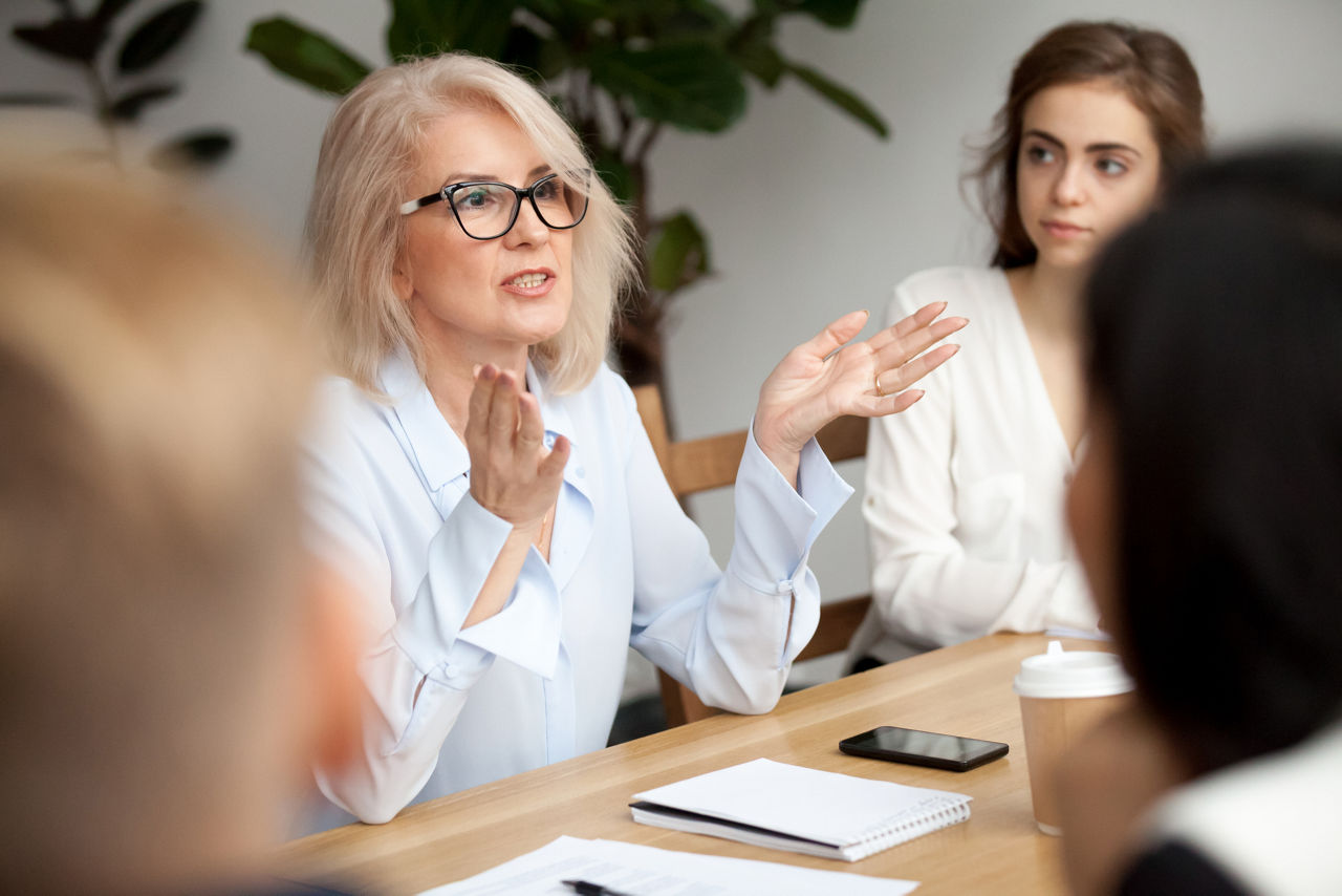 A woman at a conference table leading a discussion with employees around the table.