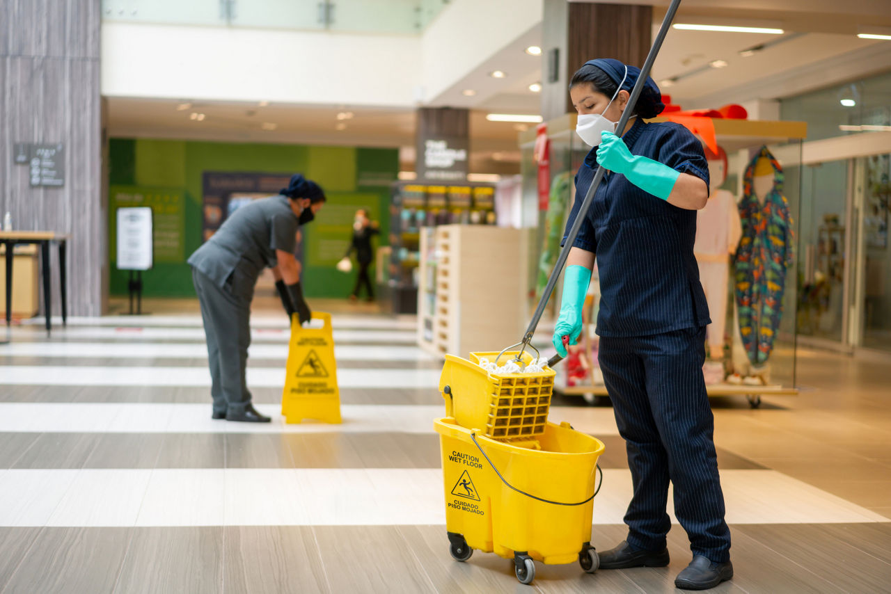 Team of Latin American cleaning ladies mopping the floor at a shopping mall and wearing facemask during the pandemic