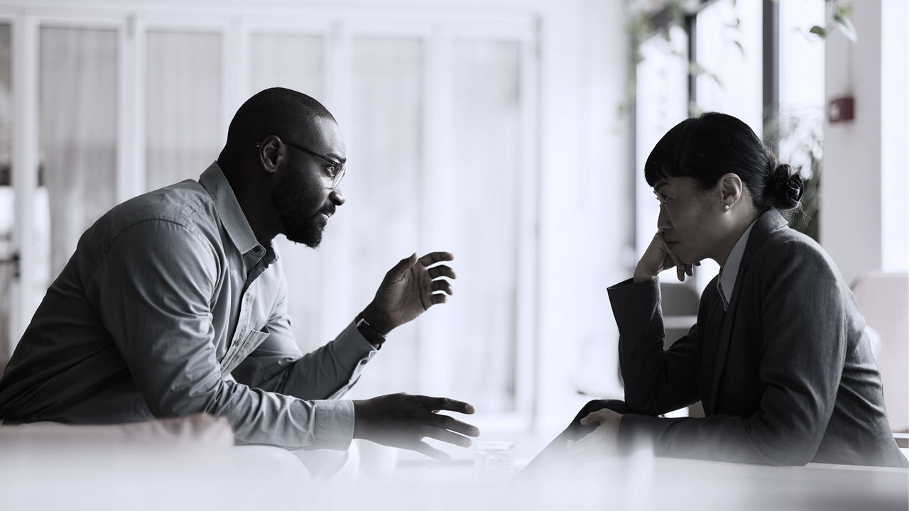 Male leader sitting on left talks to female manager sitting on right