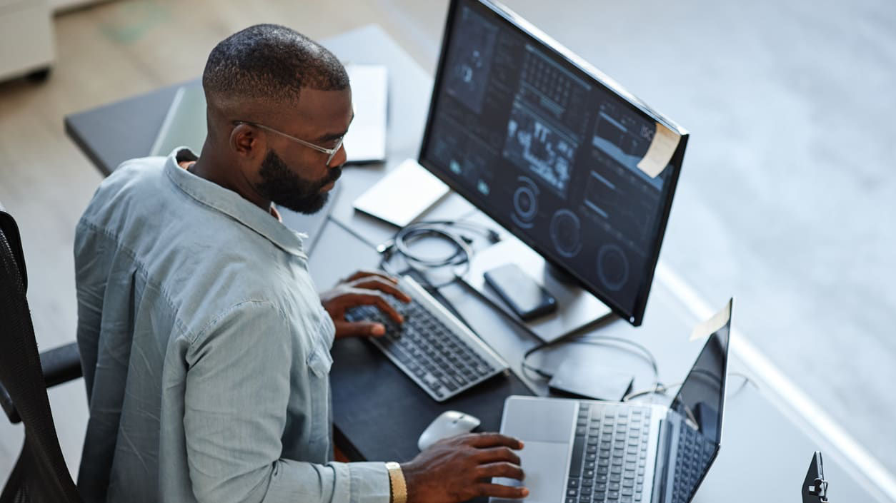 A man sitting at a desk with two laptops in front of him.