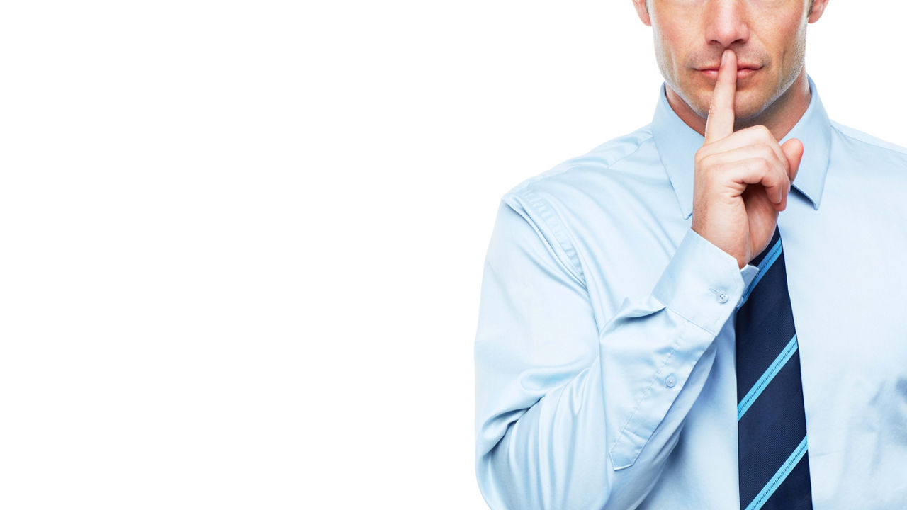 A businessman with his finger on his lips making a hush sign.