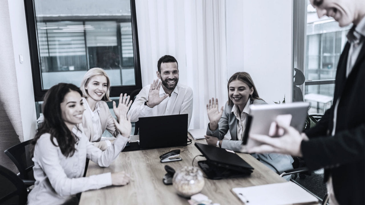 A group of business people sitting around a table and waving.