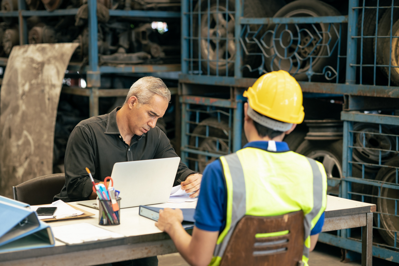 Factory manager looking at the paper with young engineer sitting front 