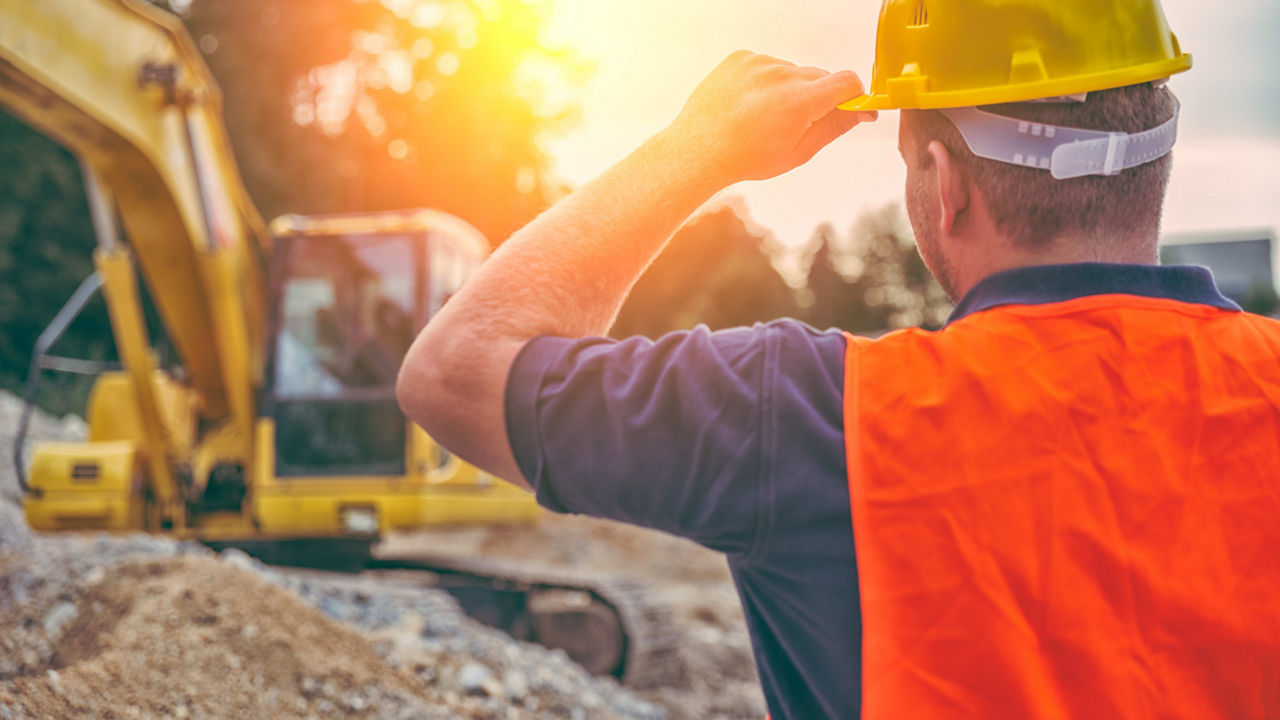 A construction worker is looking at an excavator.
