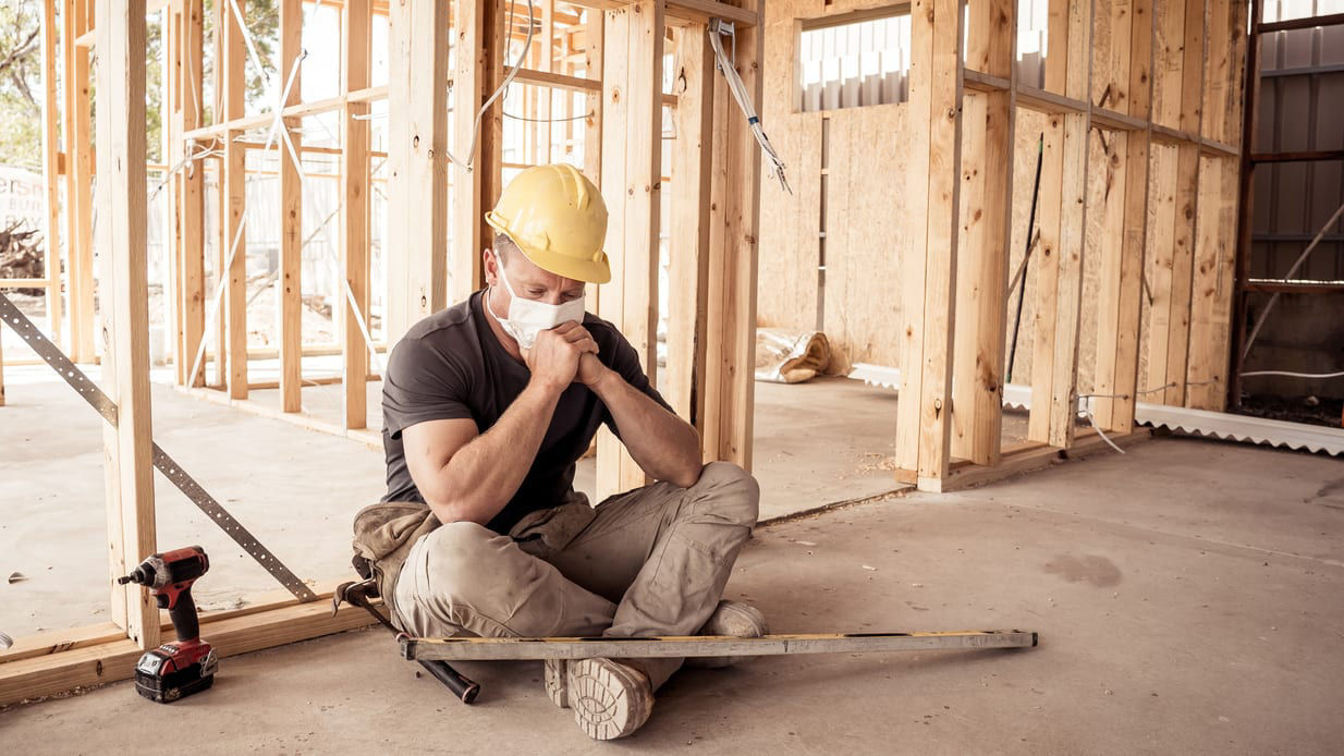 A construction worker sitting on the floor of an unfinished house.