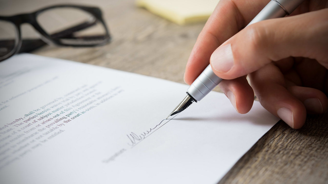 A person signing a document with a pen.