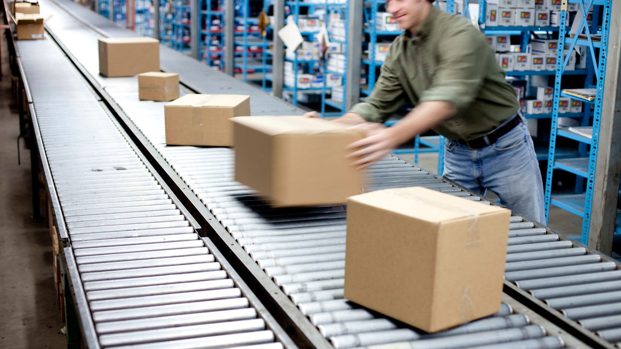A man pushing boxes on a conveyor belt in a warehouse.