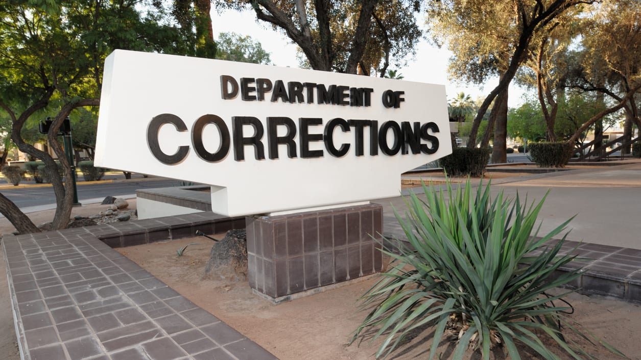 The department of corrections sign is in front of a tree.