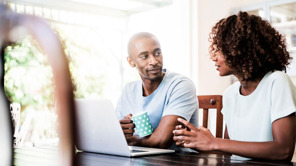 A man and woman sitting at a table looking at a laptop.