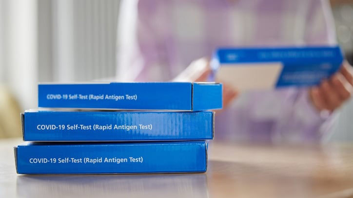 A woman is holding a stack of blue boxes on a table.