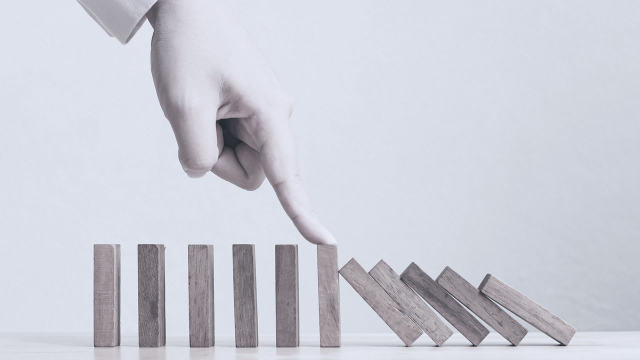 A woman's hand is pointing at a wooden dominoes tower.