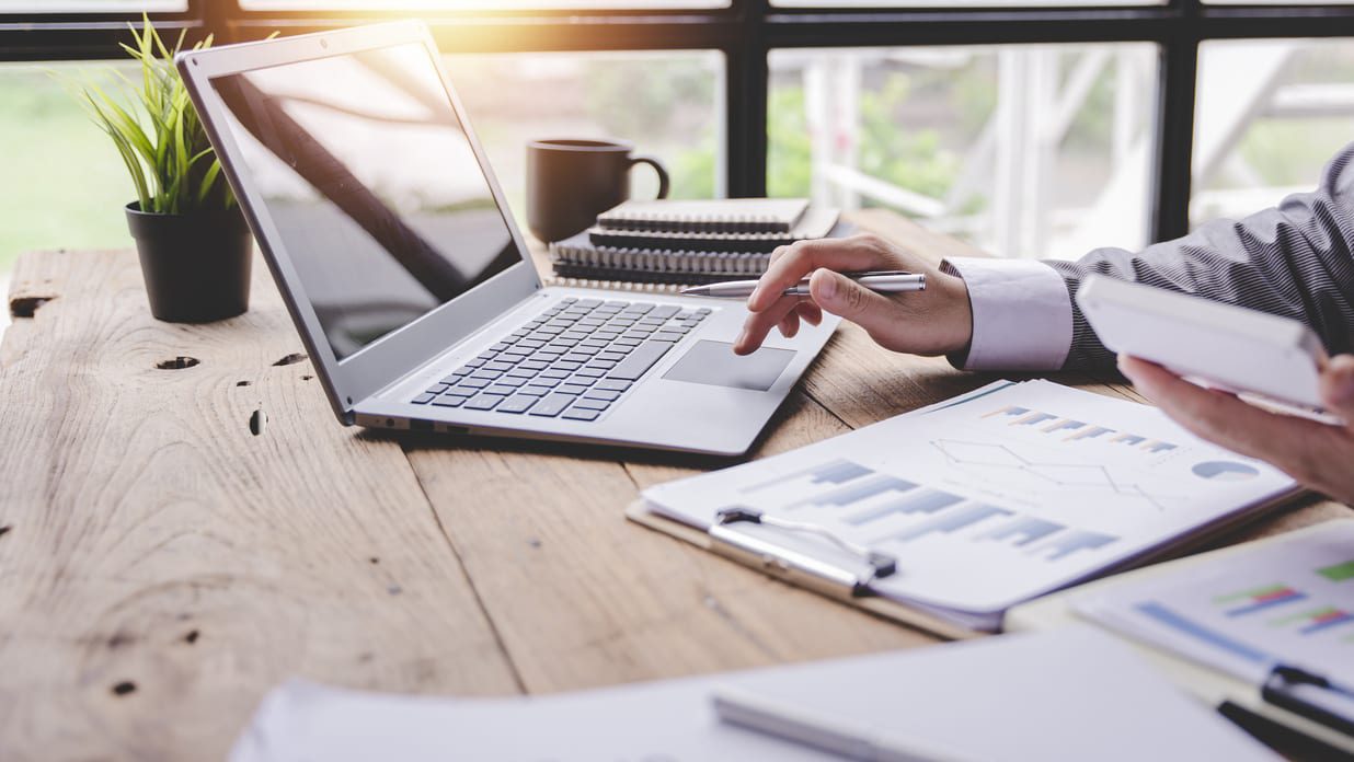 person using laptop with reports on desk