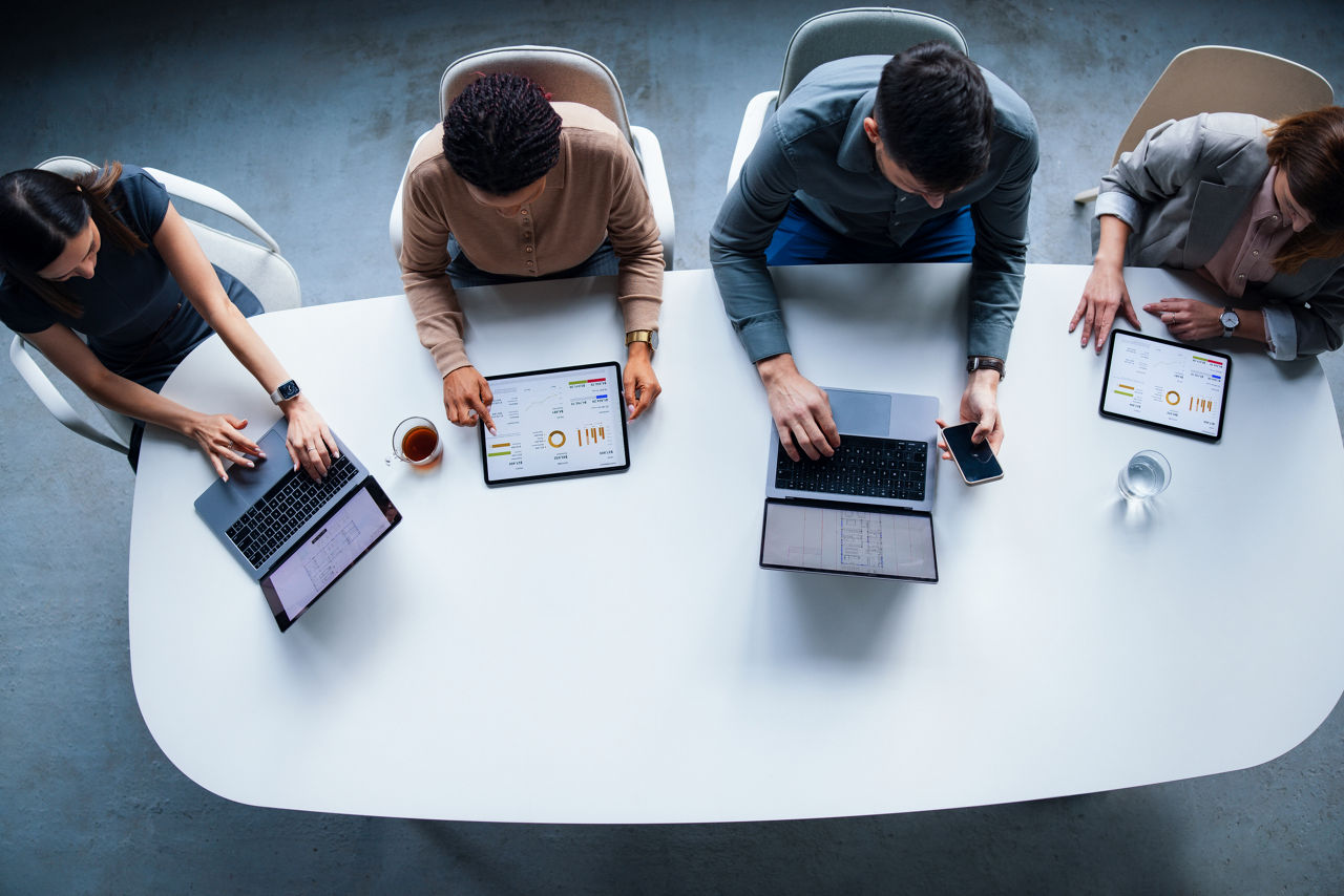 A group of professionals working together in a modern office setting using laptops and tablets, displaying teamwork, productivity, innovation, and a focus on data analysis and technology-driven collaboration.
